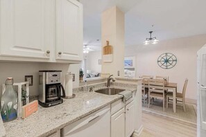 A kitchen with white cabinets, a coffee maker, a sink, and a dining area with a table and chairs.