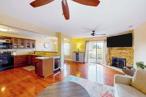 A spacious living area with a kitchen, a fireplace, and a ceiling fan. - Eagles Landing home with pool and tennis access, fireplace, grill, & smart TVs (Rehoboth Beach)