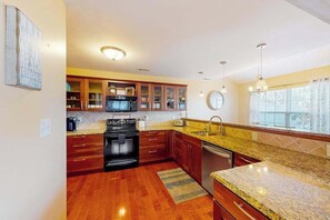 A kitchen with wooden cabinets, a black stove, a microwave, and a sink. - Eagles Landing home with pool and tennis access, fireplace, grill, & smart TVs (Rehoboth Beach)