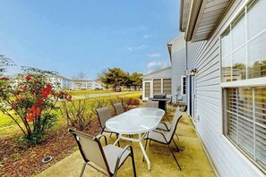 A patio with a table and chairs, a grill, and a view of a residential area. - Eagles Landing home with pool and tennis access, fireplace, grill, & smart TVs (Rehoboth Beach)