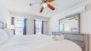 Quarto de hotel com uma cama grande, um ventilador de teto, uma cômoda e um espelho amplo.