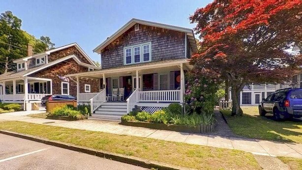 Een tweelaags huis met een veranda, een garage en een verzorgd gazon.