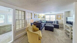Een woonkamer met een bank, een voetenbankje, een fauteuil en een televisie.