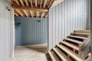 Un escalier en bois mène à une pièce dont la porte est grise et sur laquelle est inscrit le numéro « 102 ».