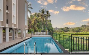 A swimming pool with a view of palm trees and a fence. - Field View 2bhk Retreat 1km to Candolim Beach (Candolim)