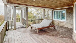 Un porche abrité avec une terrasse en bois, un lit à ossature métallique et une vue sur une maison par une fenêtre.