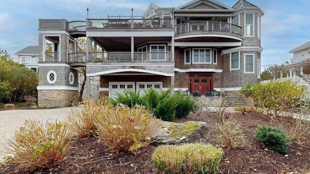 Une maison à plusieurs étages avec un balcon, un garage et un jardin aménagé à l’avant.