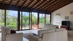 A spacious living room with large sliding glass doors, a flat-screen TV, and a ceiling with wooden beams. - Villa le Muse - beautiful detached villa with swimming pool, (Marsala)