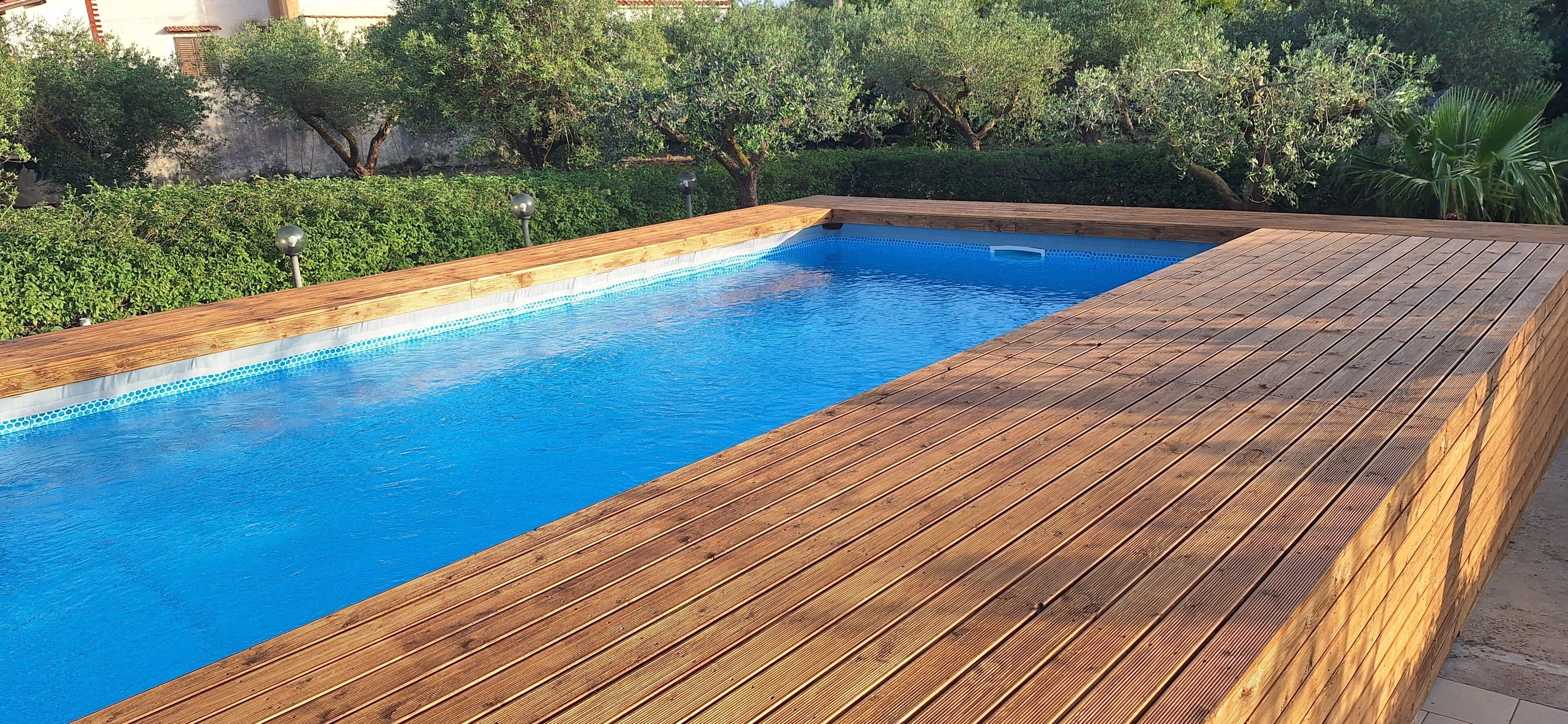 Ein rechteckiger Pool mit Holzterrasse, umgeben von viel Grün.