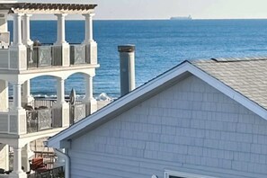 Un edificio costiero con un balcone affacciato sul mare, un camino e una nave visibile in lontananza.