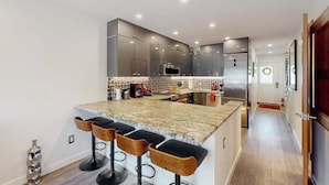 Una cocina moderna con una isla central, taburetes de bar y electrodomésticos de acero inoxidable.