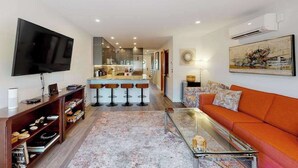 Una sala de estar con televisor, sofá, mesa de centro y una zona de bar con taburetes.