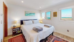 Un dormitorio con cama, mesitas de noche, alfombra, un cuadro y ventana con vistas.