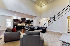 A spacious living room with a sectional sofa, a dining area, and a kitchen in the background. - Upgraded home with pools, sports courts, bikes, chef's kitchen, firepit, & gym (Rehoboth Beach)