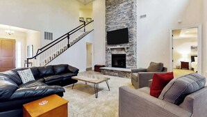 A spacious living room with a fireplace, leather sofas, a coffee table, and a staircase leading to another level. - Upgraded home with pools, sports courts, bikes, chef's kitchen, firepit, & gym (Rehoboth Beach)