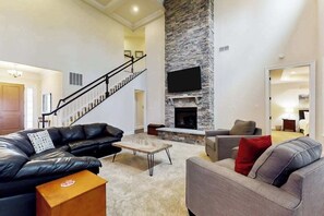 A spacious living room with a fireplace, leather sofas, a coffee table, and a staircase leading to another level. - Upgraded home with pools, sports courts, bikes, chef's kitchen, firepit, & gym (Rehoboth Beach)