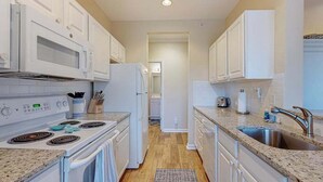 Une cuisine avec des meubles blancs, une cuisinière, un réfrigérateur, un évier et un plan de travail.