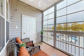 Ein überdachter Balkon mit einer weißen Tür, Korbmöbeln und Blick auf einen Parkplatz.