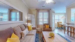 Un salon comprenant un canapé, une table basse et des fauteuils, un ventilateur de plafond et de grandes fenêtres.