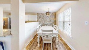 A modern kitchen with a stone backsplash, white cabinetry, and a dining area with a white table and chairs. - Eagles Landing home with gas fireplace, washer/dryer, pool & tennis court (Rehoboth Beach)