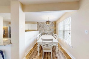 A modern kitchen with a stone backsplash, white cabinetry, and a dining area with a white table and chairs. - Eagles Landing home with gas fireplace, washer/dryer, pool & tennis court (Rehoboth Beach)
