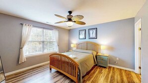 A bedroom with a wooden bed, a ceiling fan, a window with curtains, and two framed pictures on the wall. - Eagles Landing home with gas fireplace, washer/dryer, pool & tennis court (Rehoboth Beach)
