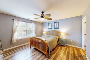 A bedroom with a wooden bed, a ceiling fan, a window with curtains, and two framed pictures on the wall. - Eagles Landing home with gas fireplace, washer/dryer, pool & tennis court (Rehoboth Beach)