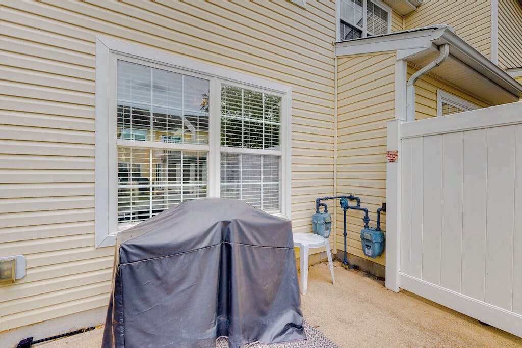 A covered outdoor grill, a window with blinds, and a water spigot on a house exterior.