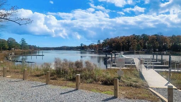 Un lago tranquilo con un muelle, rodeado de árboles y un cielo despejado.