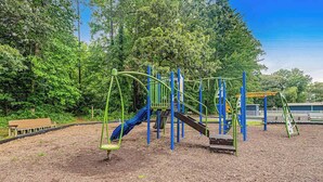 Un parque infantil con estructuras para escalar y toboganes, rodeado de árboles.