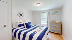 Un dormitorio con una cama, una decoración de brújula en la pared, una ventana y un pequeño aparador de madera.