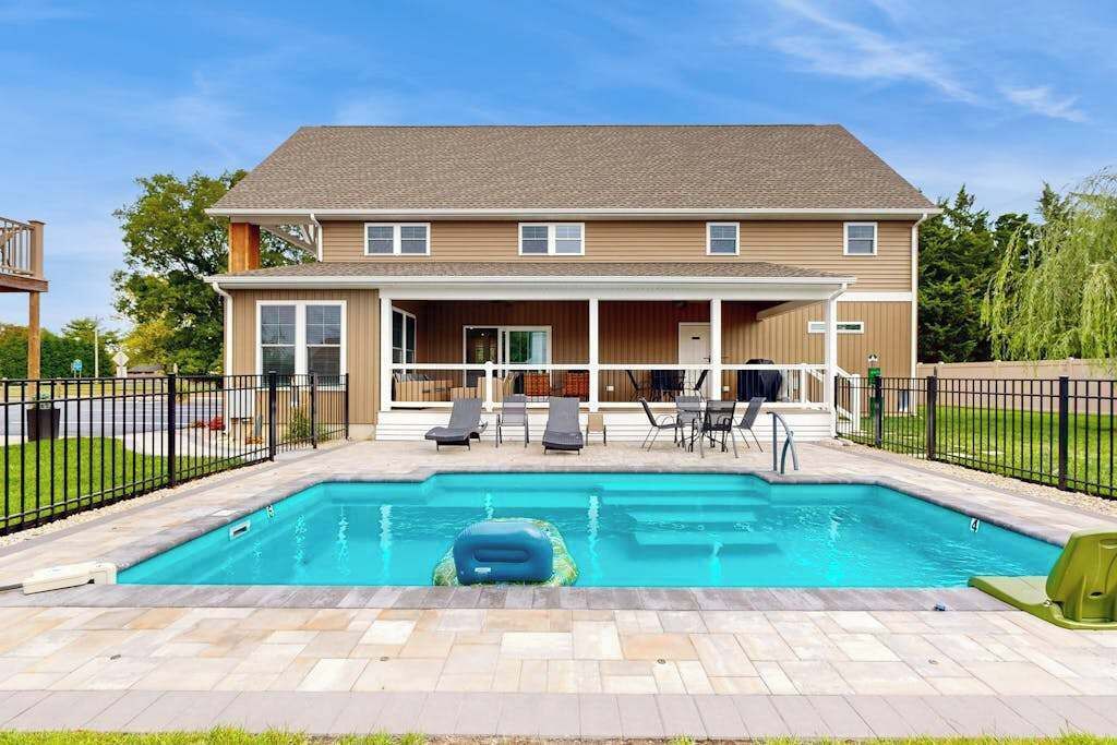 Una casa de dos pisos con piscina, mobiliario exterior y un patio vallado.