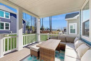 A covered outdoor patio with a wooden table and a sofa, white railings, and a view of neighboring houses. - Arbor-Lyn house with shared pool, fire pit, deck & gas grill (Rehoboth Beach)