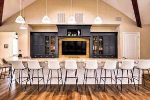 A kitchen with a bar area, dark cabinets, and a large TV. - Arbor-Lyn house with shared pool, fire pit, deck & gas grill (Rehoboth Beach)