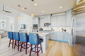A modern kitchen with a central island, bar stools, and a large refrigerator. - Arbor-Lyn house with shared pool, fire pit, deck & gas grill (Rehoboth Beach)