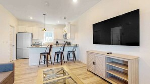 Ett modernt kök med vita skåp, en stor köksö och en platt-TV som är monterad på väggen.
