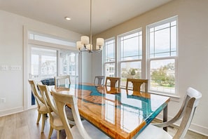 A dining area with a large glass-top table, wooden chairs, and a chandelier. - Oyster House Village house w/community pool, private hot tub, kayaks (Rehoboth Beach)