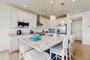A modern kitchen with white cabinetry, granite countertops, a central island with bar stools, and pendant lighting. - Oyster House Village house w/community pool, private hot tub, kayaks (Rehoboth Beach)