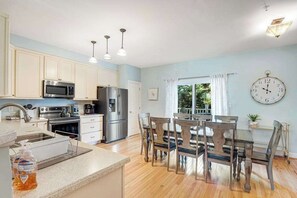 A kitchen with white cabinets, stainless steel appliances, a dining table with chairs, and a clock on the wall. - Edgewater Park townhome with pool, patio, grill, balcony, AC & beach gear (Rehoboth Beach)