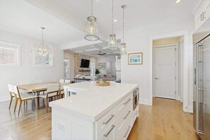 A modern kitchen with a large island, pendant lights, and a dining area with a table and chairs. - Town of Rehoboth Beach house w/private pool, patio, grill, walk to beach (Rehoboth Beach)