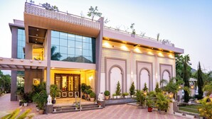 Un hotel moderno con fachada de vidrio, un acceso cubierto y un patio ajardinado con plantas en macetas.