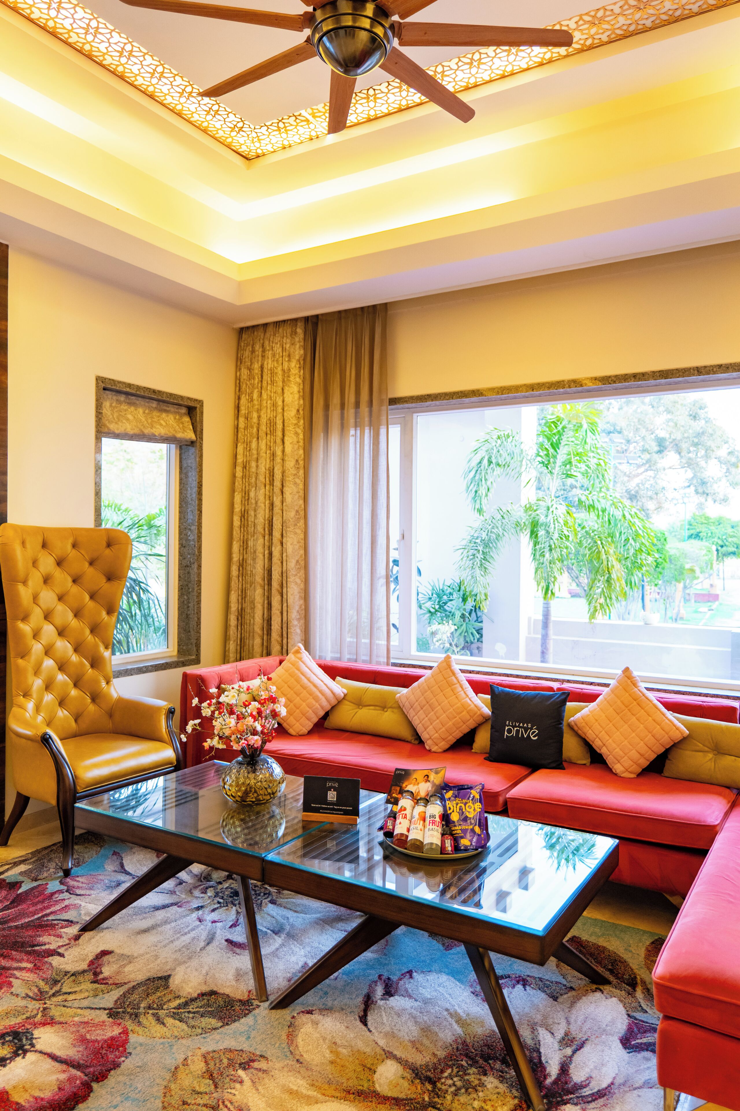 A modern living room with a glass coffee table, a red sofa, a leather armchair, and a ceiling fan.