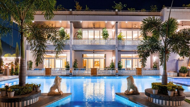 Un hotel con piscina, dos estatuas de leones y un edificio de varios pisos con balcones.