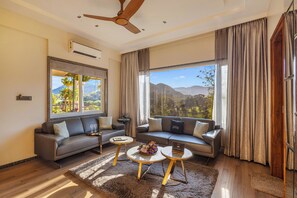 A modern living room with a sofa, two coffee tables, and a ceiling fan. - ELIVAAS Prive Mountain Creek 1 Luxe Room (Udaipur)