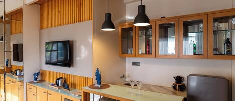 A modern kitchen with wooden cabinets, a flat-screen TV, pendant lights, and a refrigerator.