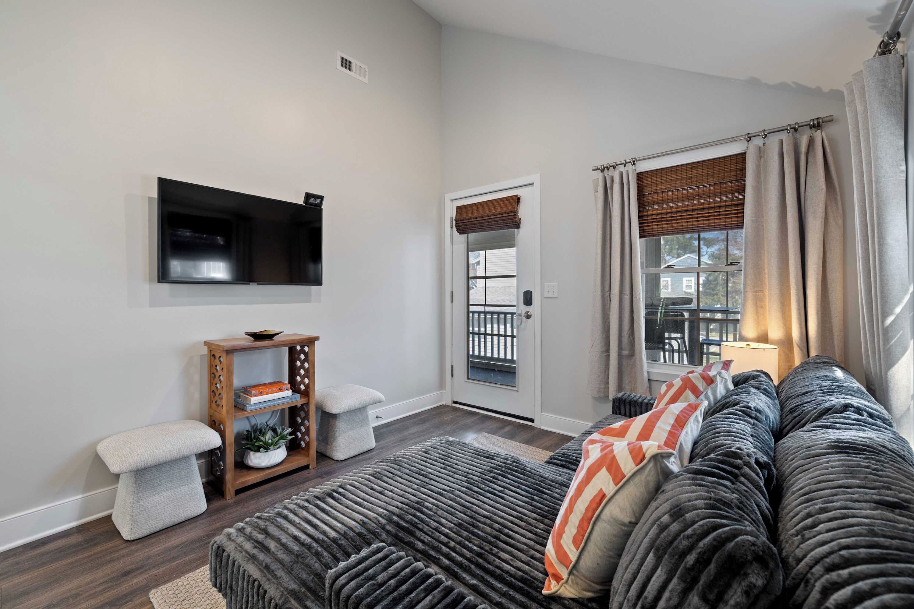 A living room with a sofa, a television mounted on the wall, a small wooden side table, and a door leading to a balcony.