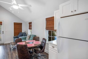 Eine moderne Küche mit einem weißen Kühlschrank, einem Esstisch mit Stühlen, einem Deckenventilator und einem Fenster mit Jalousie.