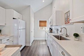 Una cocina moderna con armarios blancos, un lavamanos de acero inoxidable y un ventanal con persianas.