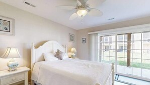 Une chambre à coucher avec un lit, des lampes de chevet, un ventilateur de plafond et une grande fenêtre donnant sur un beau paysage.