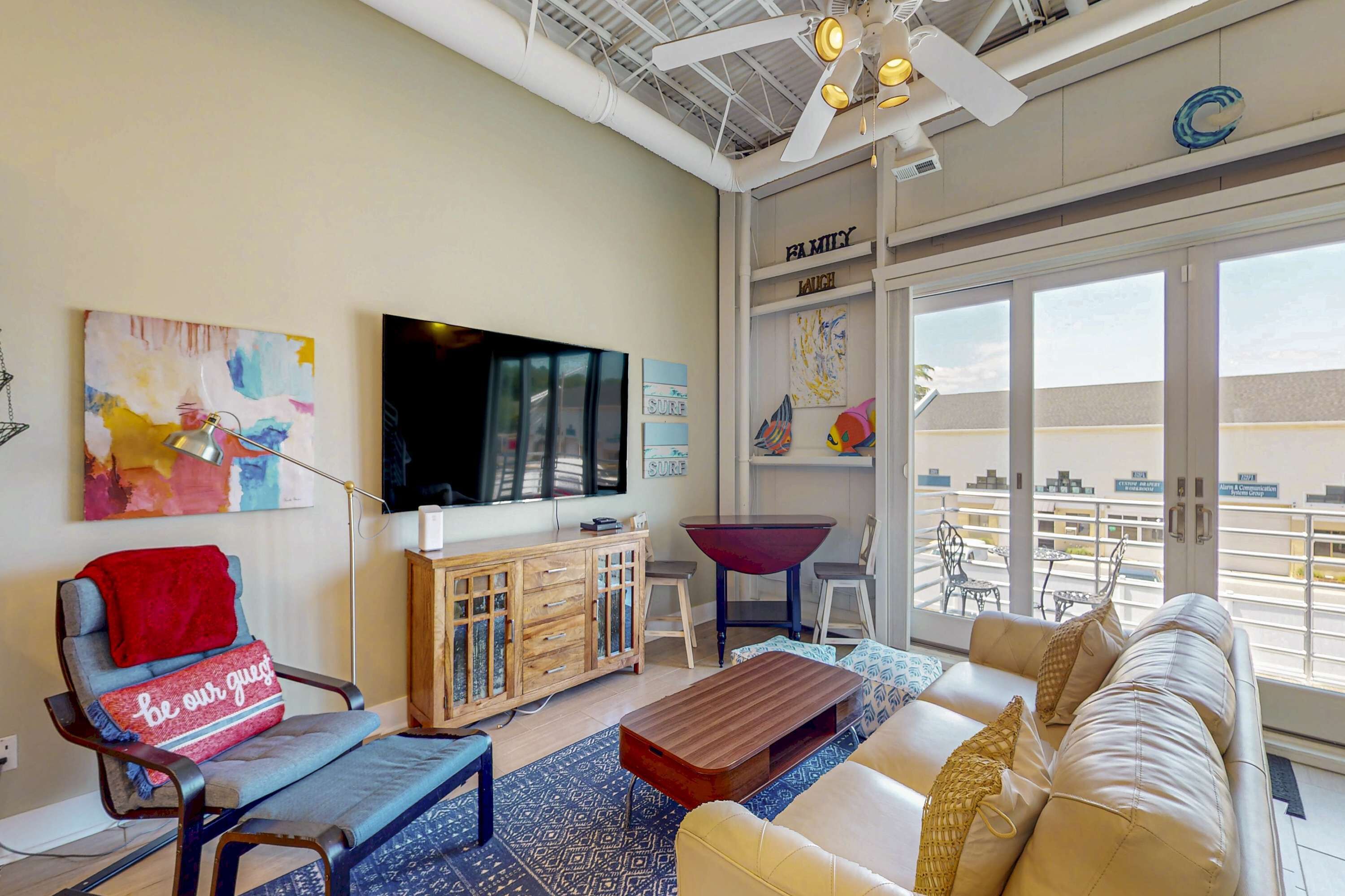A modern living room with a sofa, a coffee table, a TV, a wooden cabinet, and a balcony with outdoor furniture.